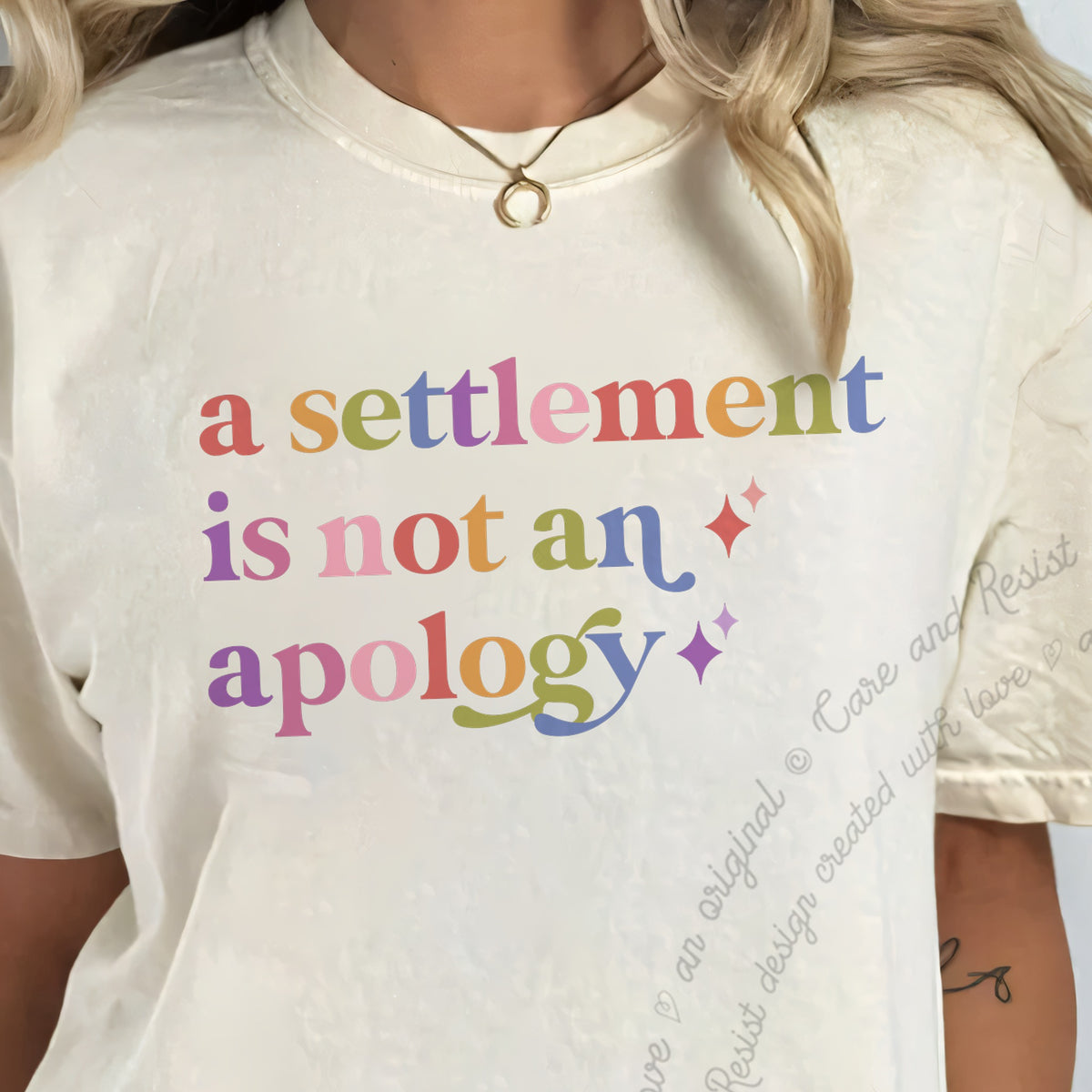 A Settlement is not an Apology Care & Resist tee in Ivory, close-up of the lettering